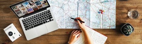Camera, laptop, persons hand on map and coffee cup on table