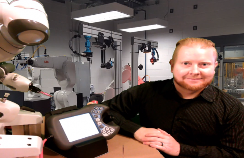 Thomas Forget delivers online lectures from his garage with a photo of one of St. Clair College’s robotics labs behind him. Next to him is the ABB YuMi robot he uses to demonstrate. 
