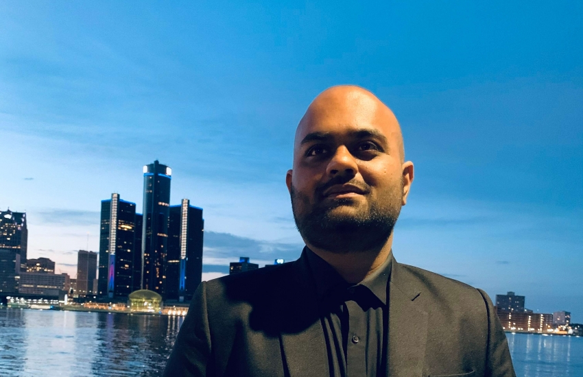 Kushal Patel standing in front of the Detroit river with the GM Renaissance Center in the background.