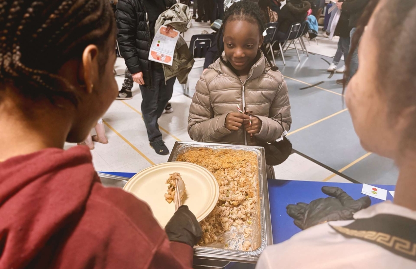 Two volunteers dish out prepared menu items to a student