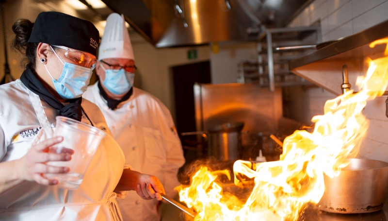 Culinary & Hospitality Management student cooking with fire on the stove.