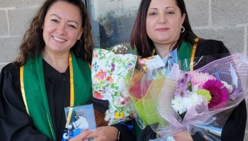 Female students in graduation gowns with flowers and stuffed animals