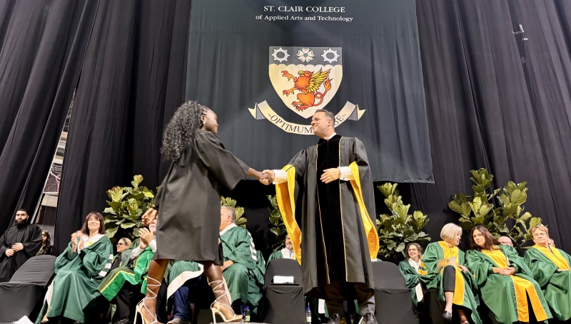 Student shaking hands with Michael Silvaggi on stage. Faculty and staff seated behind.